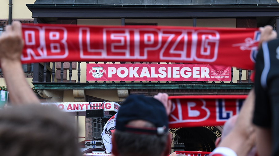 Am Rathausbalkon in Leipzig hängt ein Schild mit der Aufschrift «Pokalsieger», davor hält ein Fan einen Schal mit dem Schriftzug «RB Leipzig». / Foto: Robert Michael/dpa/Archivbild