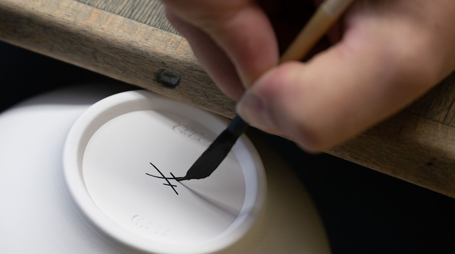 Die gekreuzten Schwerter, das Markenzeichen der Porzellan-Manufaktur Meissen, werden auf den Boden einer Kanne gemalt. / Foto: Sebastian Kahnert/dpa/Archivbild