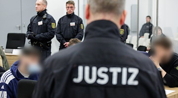 Ein Justizbeamter beobachtet zwei der Angeklagten im Gerichtssaal. / Foto: Jens Schlueter/AFP/POOL/dpa/Archivbild