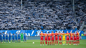 Spieler und Schiedsrichter stehen für eine Schweigeminute auf dem Spielfeld. / Foto: Swen Pförtner/dpa