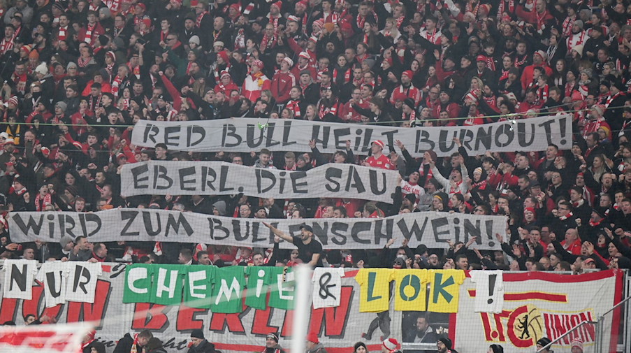 Fans von Union Berlin halten Banner mit der Aufschrift "Red Bull heilt Burnout! Eberl, die Sau. Wird zum Bullenschwein!". / Foto: Robert Michael/dpa/Archivbild