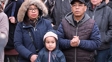 Hoa Nguyen, Tochter Emilia und Pham Phi Son, eine vietnamesische Familie aus Chemnitz, steht bei einer Kundgebung beisammen. / Foto: Sebastian Willnow/dpa