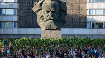 Teilnehmer einer Kunstperformance halten in der Innenstadt von Chemnitz Zimmerpflanzen vor dem Karl-Marx-Monument, dem Wahrzeichen der Stadt, in die Höhe. / Foto: Hendrik Schmidt/dpa/Archivbild