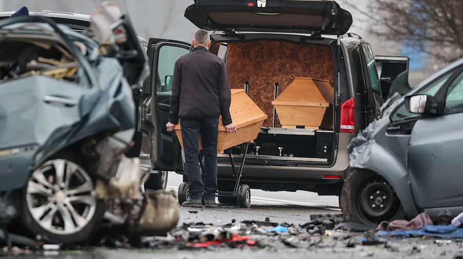 Ein Bestatter schiebt den Sarg eines Unfalltoten nach einem schweren Verkehrsunfall auf der B87 in den Bestattungswagen. / Foto: Jan Woitas/dpa