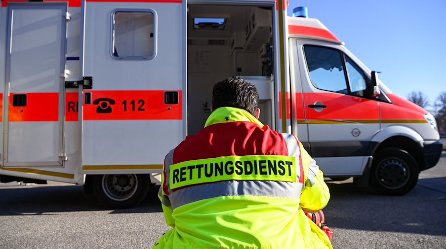 «Rettungsdienst» steht auf der Jacke eines Mannes vor einem Rettungswagen der Feuerwehr. / Foto: Jens Kalaene/dpa/Symbolbild
