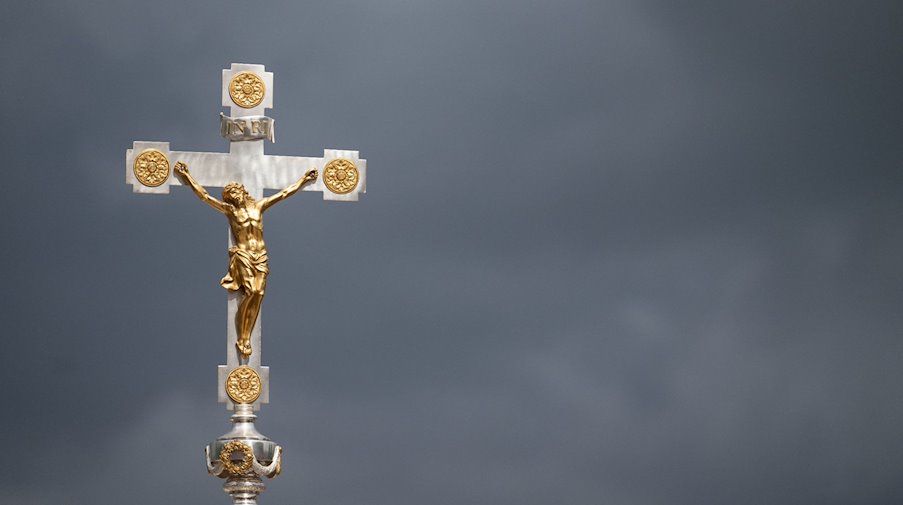 Ein katholisches Kruzifix ist vor dunklen Wolken zu sehen. / Foto: Marijan Murat/dpa/Symbolbild