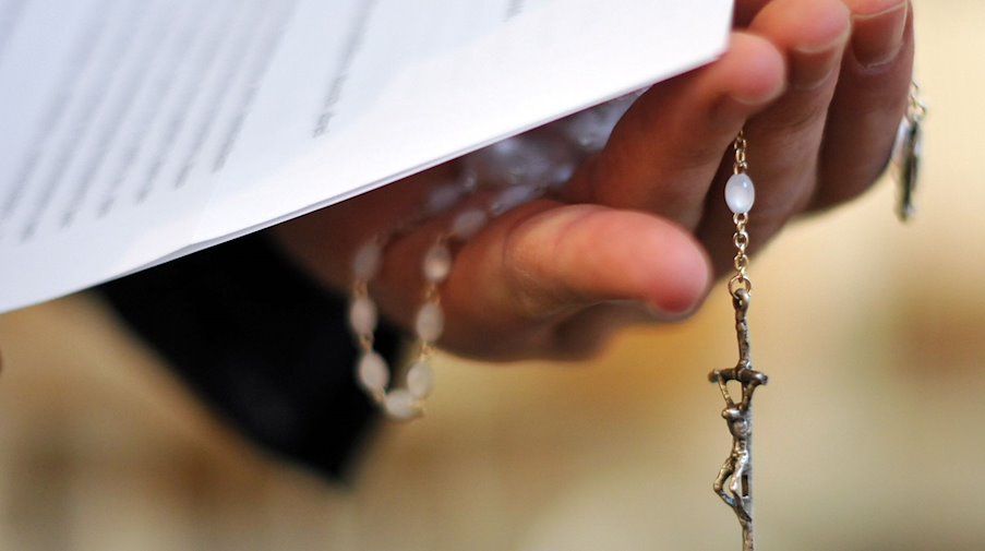 Ein Priester hält einen Rosenkranz und eine bischöfliche Erklärung in der Hand. / Foto: picture alliance / dpa/Archivbild
