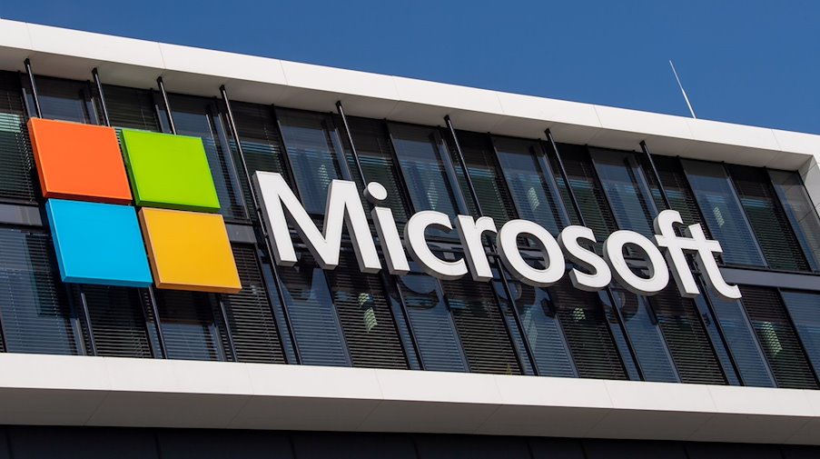 Das Microsoft Logo hängt an der Fassade eines Bürogebäudes. / Foto: Peter Kneffel/dpa/Archivbild