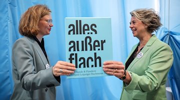 Die Kuratorinnen Bettina Baltschev (l) und Margot Dijkgraaf stehen mit dem Motto des Gastlandes 2024 „alles außer flach“ auf der Leipziger Buchmesse. / Foto: Jan Woitas/dpa