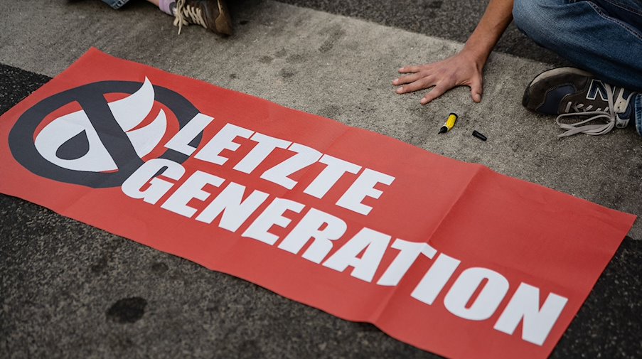 Ein Aktivist der Gruppe «Letzte Generation», der seine Hand selbst auf der Straße festgeklebt hat, blockiert eine Kreuzung. / Foto: Swen Pförtner/dpa/Archivbild