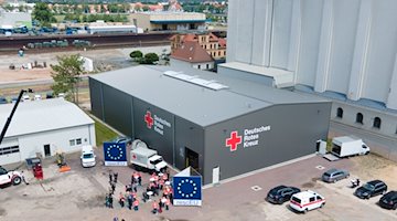 Teilnehmer eines Pressetermins zur Eröffnung des neuen Logistikzentrums des Deutschen Roten Kreuz (DRK) stehen vor der neuen Lagerhalle. / Foto: Sebastian Kahnert/dpa