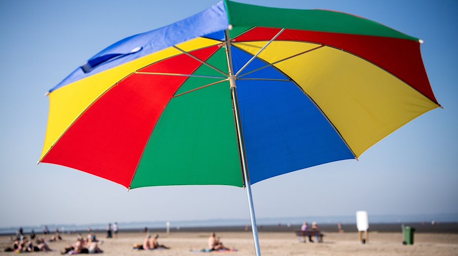 Ein bunter Sonnenschirm steht am Strand. / Foto: Sina Schuldt/dpa/Symbolbild