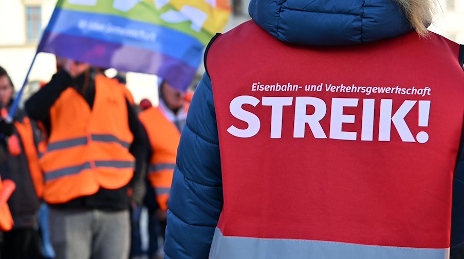 «Streik!» steht auf der Warnweste einer Teilnehmerin am Warnstreik vor dem Erfurter Hauptbahnhof. / Foto: Martin Schutt/dpa/Archivbild