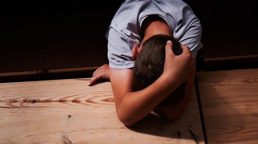 Ein Kind versteckt sein Gesicht unter seinen Armen und liegt mit dem Kopf auf einem Tisch. / Foto: Annette Riedl/dpa/Illustration