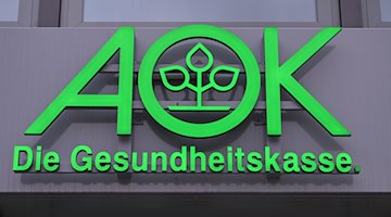 Das Logo der AOK, Allgemeine Ortskrankenkasse, ist an einem Gebäude zu sehen. / Foto: Patrick Pleul/dpa-Zentralbild/ZB