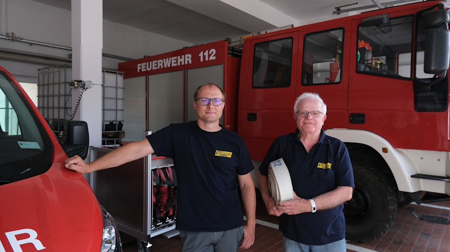 Christian Rothe (l) und Klaus Grabein, Mitglieder der Freiwilligen Feuerwehr, stehen im Gerätehaus. / Foto: Sebastian Willnow/dpa