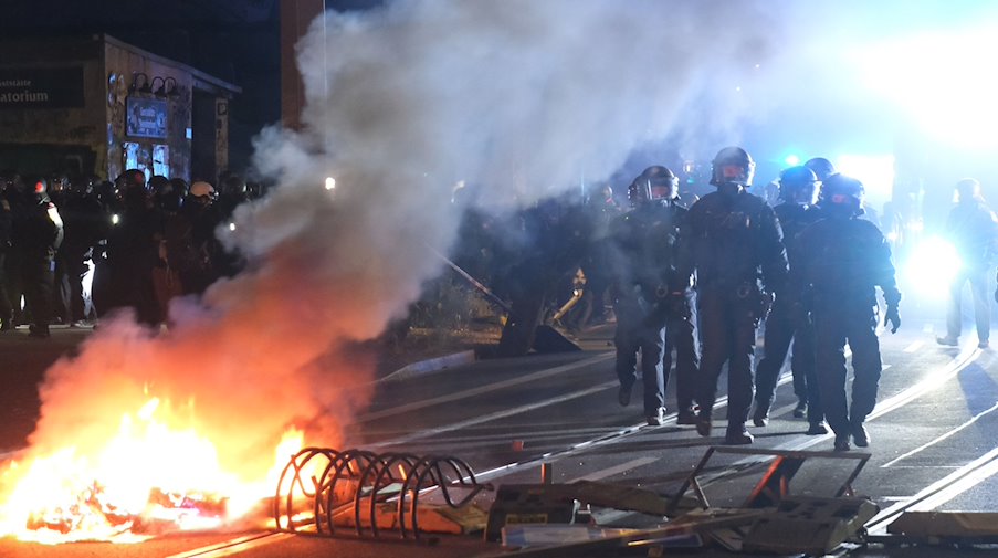 Polizisten gehen an einer brennenden Barrikade vorbei. / Foto: Sebastian Willnow/dpa