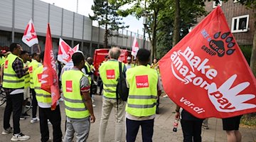 Beschäftigte von Amazon stehen bei einer Demonstration unter dem Titel "Make Amazon Pay! Für gute und gesunde Arbeit bei Amazon!" in Hamburg-Veddel. / Foto: Christian Charisius/dpa