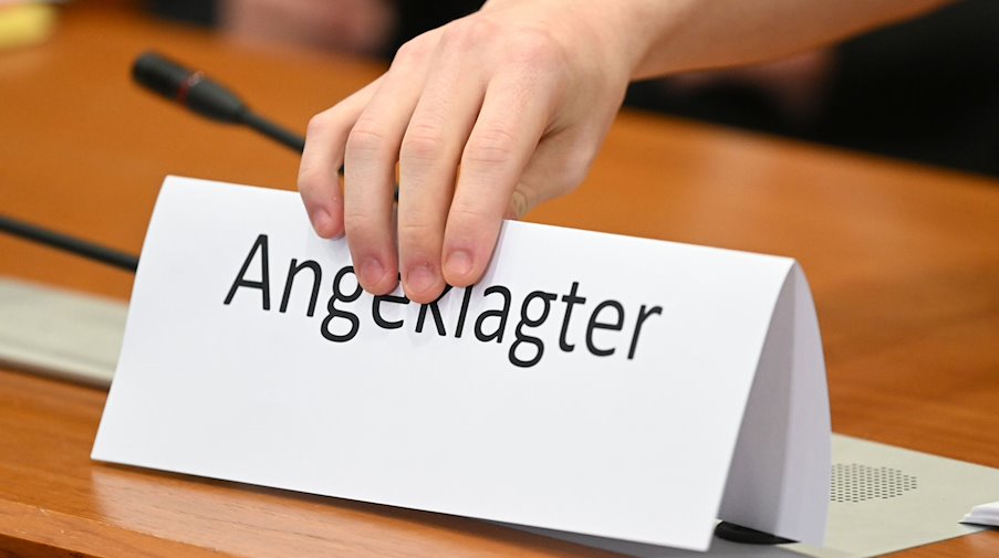 Ein Schild mit der Aufschrift "Angeklagter" wird auf die Gerichtsbank gestellt. / Foto: Arne Dedert/dpa/Symbolbild