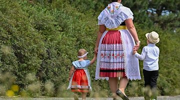 Eine Mutter in sorbisch-wendischer Festtagstracht geht mit ihren Kindern in Heinersbrück spazieren. / Foto: Patrick Pleul/dpa