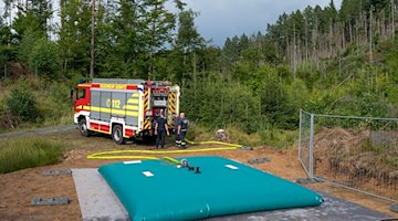 Feuerwehrmänner befüllen die erste mobile Löschwasserzisterne im Nationalpark Sächsische Schweiz. / Foto: Matthias Rietschel/dpa