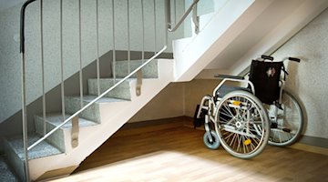 Ein Rollstuhl steht unter einer Treppe in einem Wohnhaus. / Foto: Arno Burgi/zb/dpa