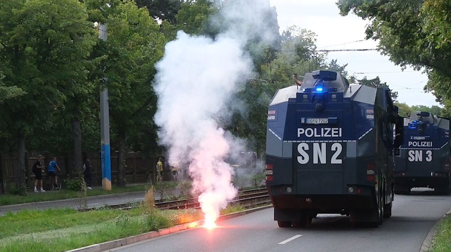 Pyrotechnik zündet auf einer Straße, während Wasserwerfer der Polizei vorüberfahren. / Foto: Sebastian Willnow/dpa