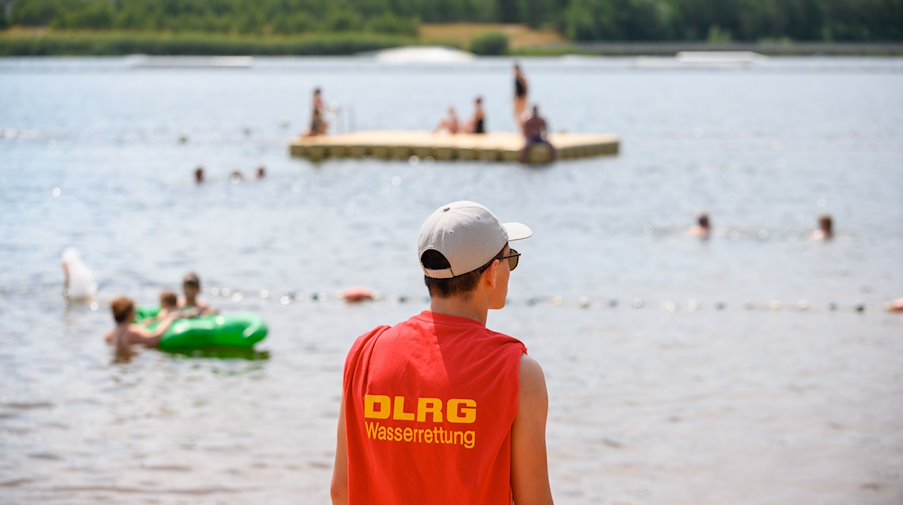 Ein Mitglied der Deutschen Lebens-Rettungs-Gesellschaft (DLRG) steht in einem Strandbad am Ufer. / Foto: Jonas Walzberg/dpa/Symbolbild