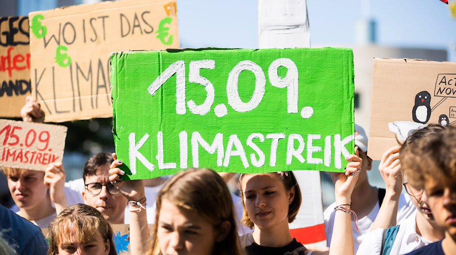 Ein Schild mit der Aufschrift «15.09. Klimastreik» wird in die Höhe gehalten. / Foto: Christoph Soeder/dpa