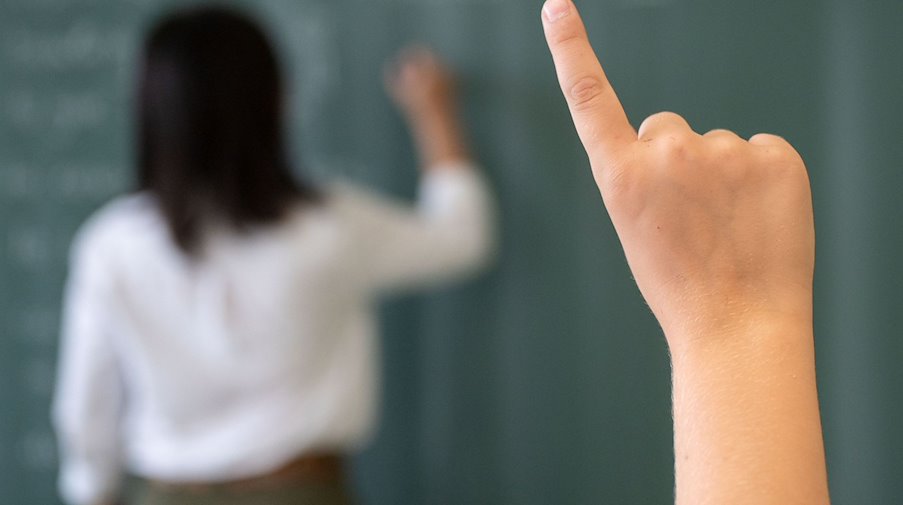 Ein Schüler meldet sich, während die Lehrerin an die Tafel schreibt. / Foto: Marijan Murat/dpa/Symbolbild