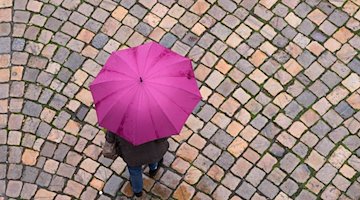 Eine Frau geht mit einem Regenschirm auf einer Straße entlang. / Foto: Sebastian Kahnert/dpa-Zentralbild/dpa/Symbolbild