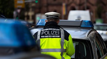 Un agente de policía entre dos vehículos policiales / Foto: Philipp von Ditfurth/dpa/Symbolbild