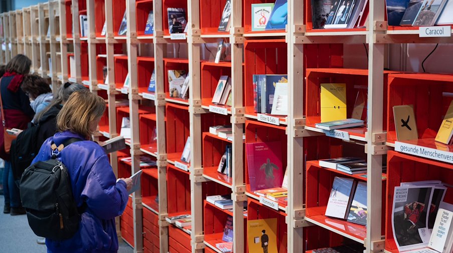 Besucherinnen und Besucher der Leipziger Buchmesse blättern in Büchern an einem Stand. / Foto: Hendrik Schmidt/dpa