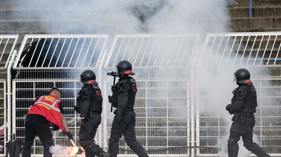 Un guardia de seguridad apaga material pirotécnico junto a agentes de policía en el estadio Bruno Plache / Foto: Hendrik Schmidt/dpa