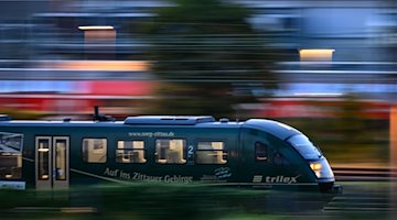 Ein Trilex Zug der Länderbahn fährt am Morgen auf einem Gleis entlang. / Foto: Robert Michael/dpa