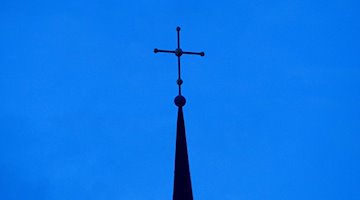 Das Kreuz einer Kirche ist in der Abenddämmerung zu sehen. / Foto: Friso Gentsch/dpa/Symbolbild