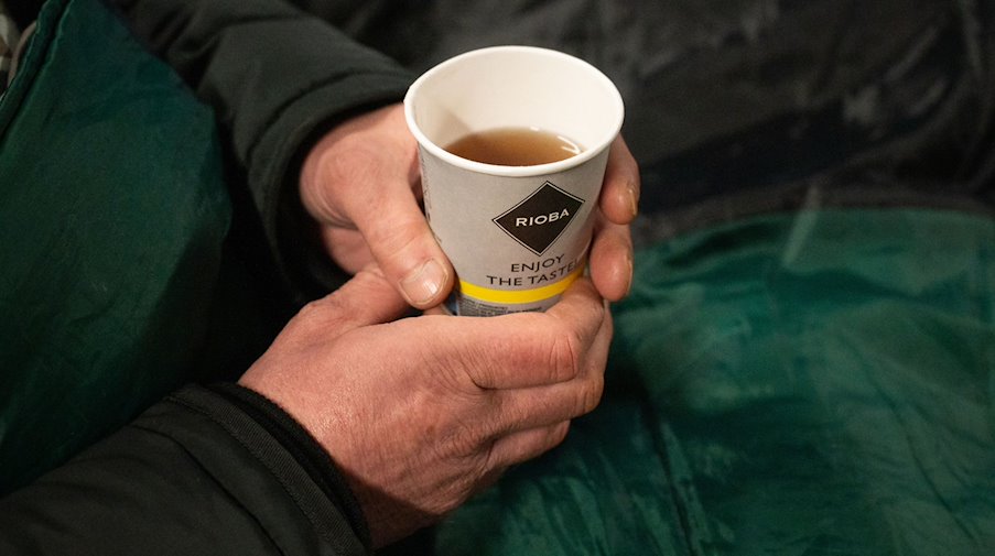 Ein Obdachloser hält einen Becher Tee in der Hand. / Foto: Christophe Gateau/dpa/Symbolbild