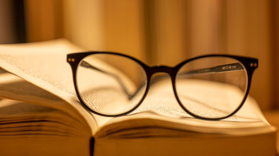 Пара окулярів для читання лежить на відкритій паперовій книзі / Фото: Monika Skolimowska/dpa/Illustration