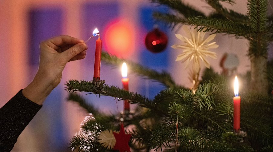 Eine Frau zündet eine Kerze an einem Weihnachtsbaum an. / Foto: Marijan Murat/dpa