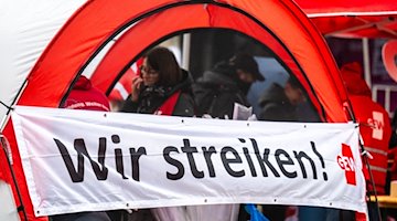 Ein Banner mit der Aufschrift „Wir streiken!“ ist bei einer Warnstreikkundgebung zu sehen. / Foto: Kristin Schmidt/dpa-Zentralbild/dpa/Archivbild