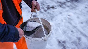 An employee of the winter road clearance service distributes road salt on a footpath. / Photo: Jan Woitas/dpa/Symbolic image