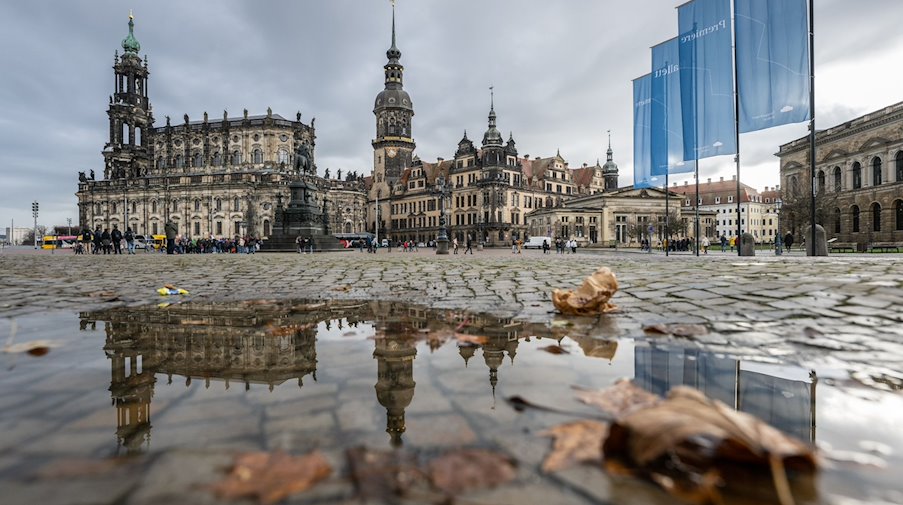 Die Hofkirche (l-r), der Hausmannsturm und das Residenzschloss spiegeln sich auf dem Theaterplatz in einer Pfütze. / Foto: Robert Michael/dpa