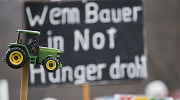 "Cuando el hambre amenaza a los agricultores necesitados" se sitúa detrás de un tractor de juguete durante una manifestación de protesta / Foto: Sebastian Christoph Gollnow/dpa