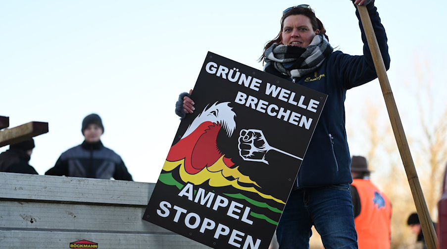 "Grüne Welle brechen, Ampel stoppen" steht auf einem Plakat der Bewegung "Land schafft Verbindung" (LSV) das Melanie Neelen, Landwirtin aus der Region, in der Hand hält. / Foto: Lars Penning/dpa