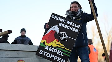 "Grüne Welle brechen, Ampel stoppen" steht auf einem Plakat der Bewegung "Land schafft Verbindung" (LSV) das Melanie Neelen, Landwirtin aus der Region, in der Hand hält. / Foto: Lars Penning/dpa