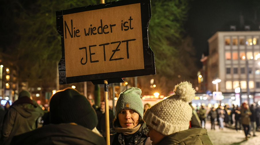 Eine Frau trägt ein Schild mit der Aufschrift «Nie wieder ist jetzt». / Foto: Oliver Berg/dpa