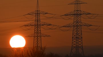 El sol sale detrás de las torres de alta tensión / Foto: Martin Schutt/dpa
