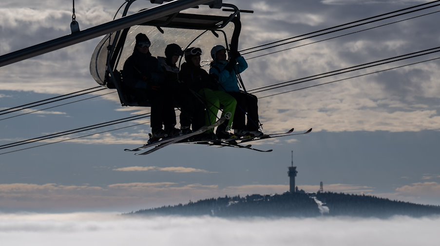 Wintersportler sitzen mit ihren Ski über den Wolken vor der Kulisse des 1243 Meter hohen Keilbergs in einem Lift und fahren auf den Gipfel des Fichtelbergs. / Foto: Hendrik Schmidt/dpa