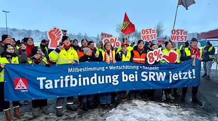 Mitarbeiterinnen und Mitarbeiter des Schrott- und Recycling-Betriebs SRW stehen mit einem Banner vor dem Werk in Rötha. / Foto: Frank Schnelle/IG Metall/dpa