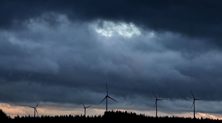 Windräder stehen bei Aitrang im Allgäu unter dichten Regenwolken hinter einem Wald. / Foto: Karl-Josef Hildenbrand/dpa